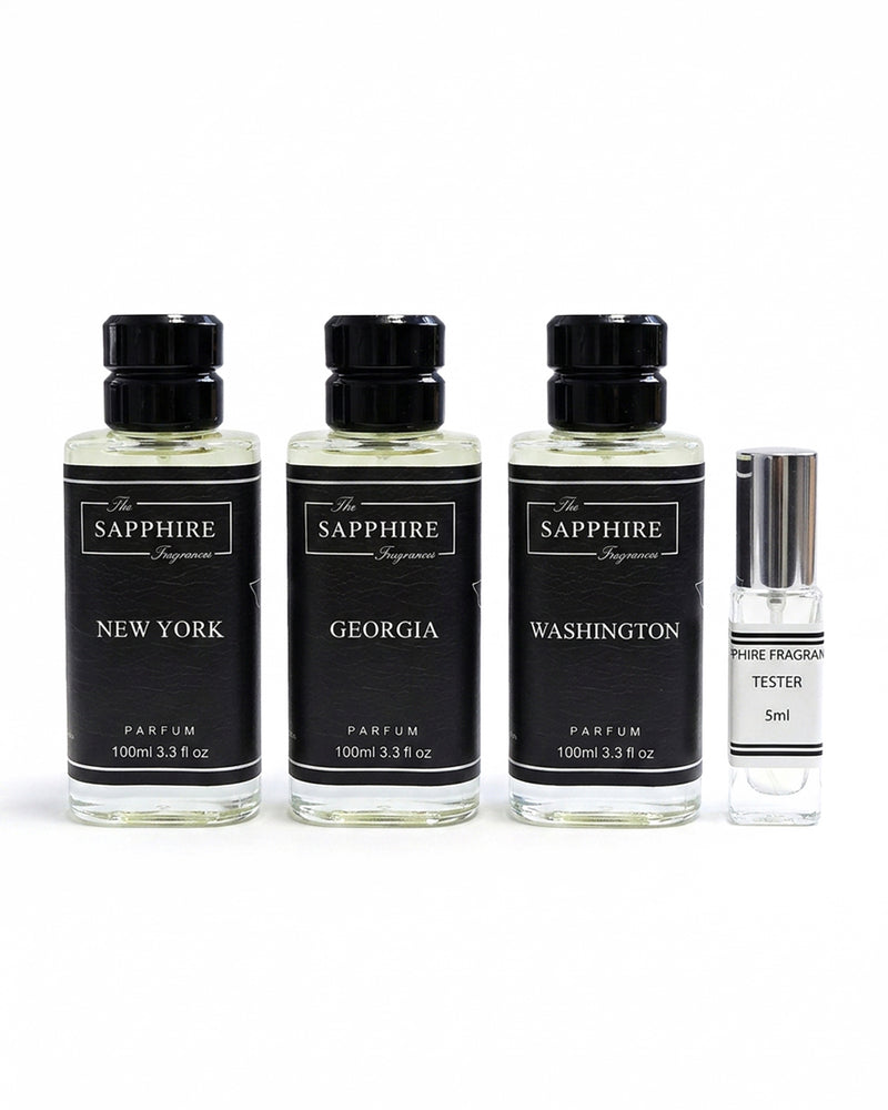 Three clear glass perfume bottles with black caps and black labels reading New York, Georgia, and Washington, alongside a small clear glass tester bottle with a silver cap, all on a white background. The labels also show The Sapphire Fragrance.